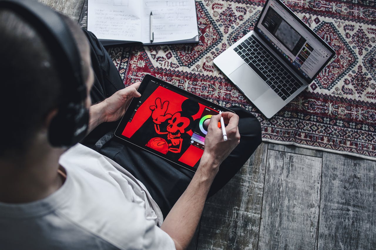 Person using a digital tablet for drawing and design work at home with a laptop.